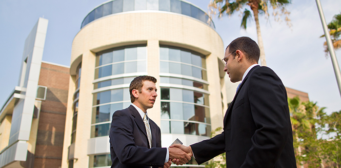 Two businesspeople shaking hands with the college in the background.