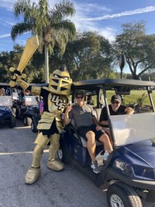 UCF mascot and two golfers in a golf cart